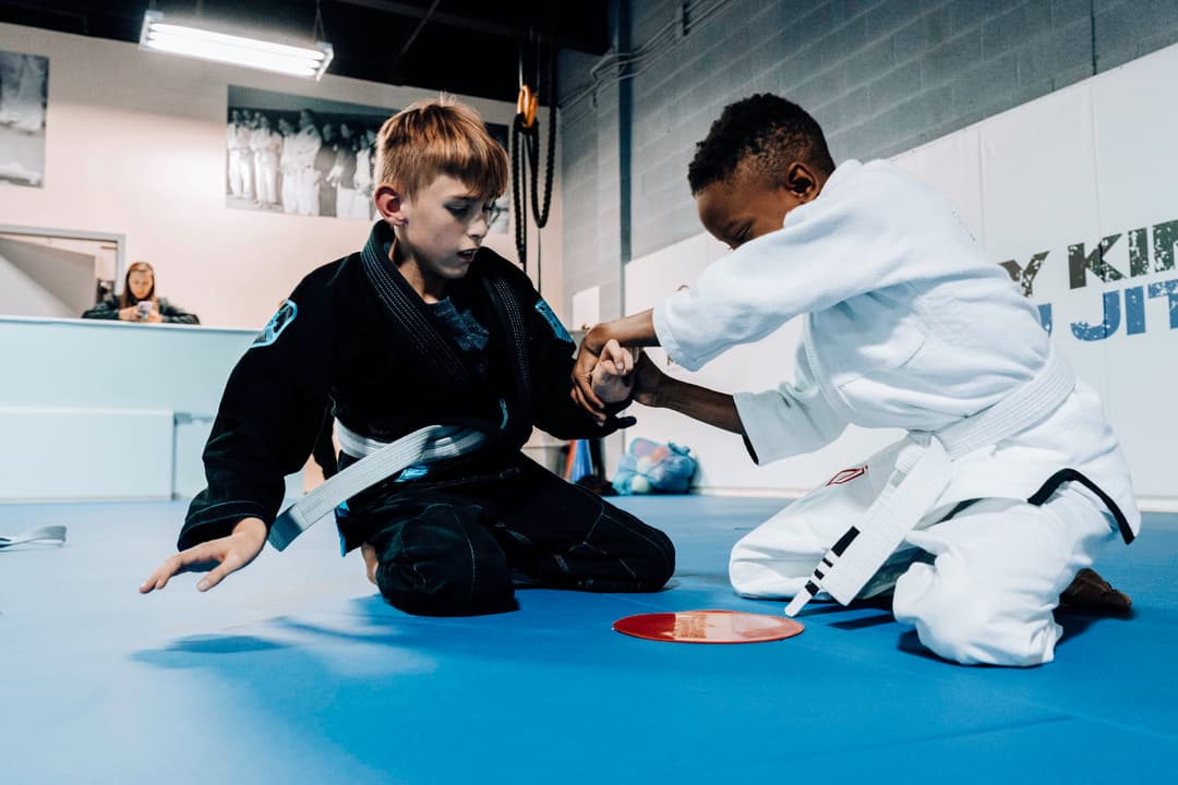 Brazilian Jiu Jitsu Kids at Kenny Kim BJJ in Marietta GA rolling on the mats with gi's on and practicing new grappling techniques